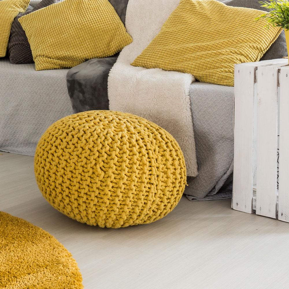 Gemütliches Wohnzimmer mit gelbem Strickhocker, Sofa mit Kissen und modernen Wohnaccessoires